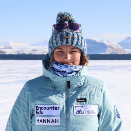 Hannah is standing with an artic backdrop. She is wearing a light blue coat and a hat.